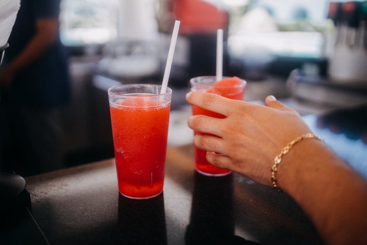 Close-up of a hand reaching for a red slushie drink in a restaurant setting.