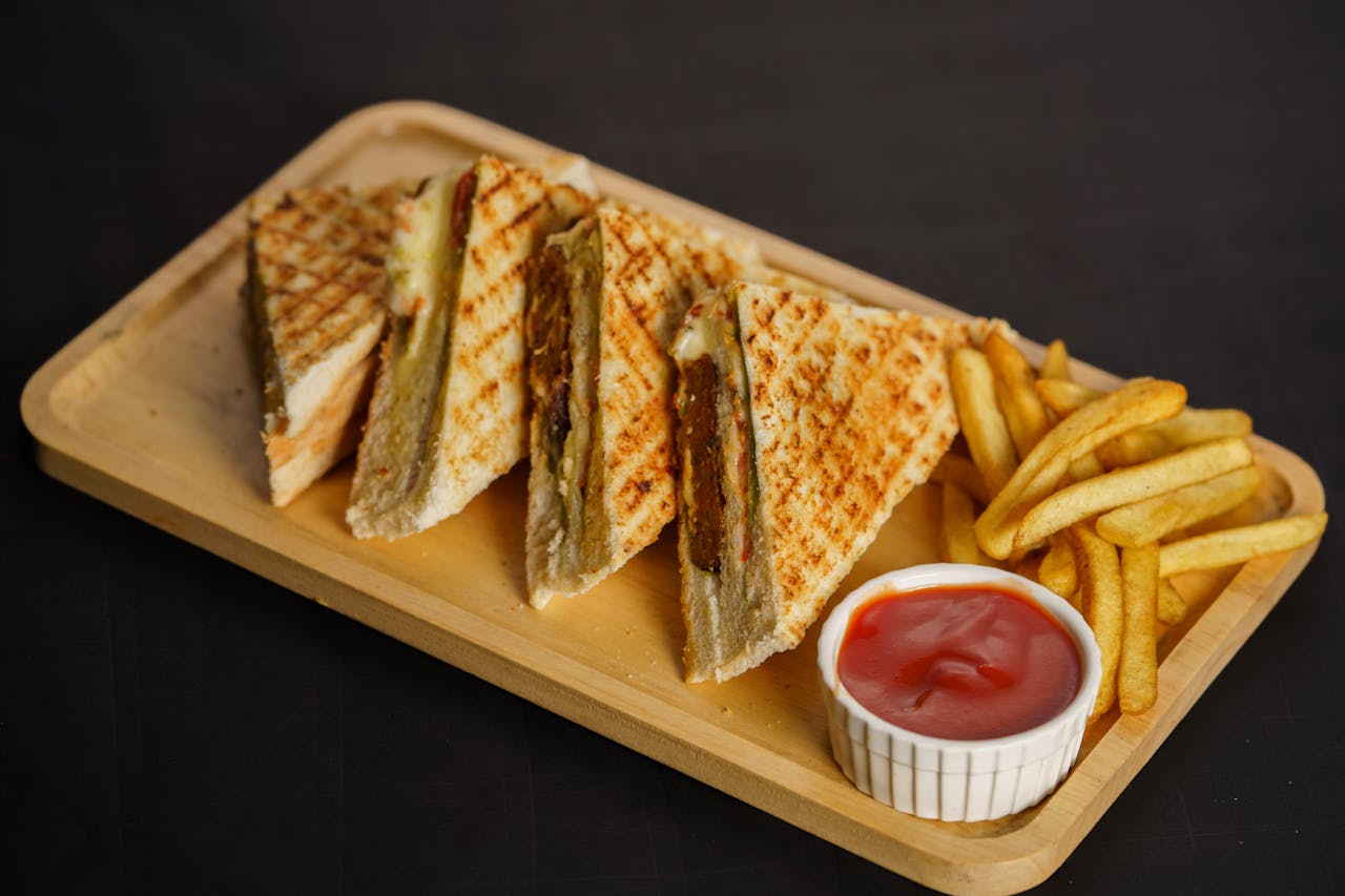 Grilled sandwich with crispy fries and ketchup on a wooden platter.